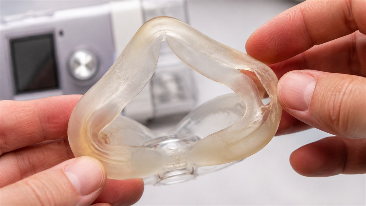 Mãos segurando a almofada de silicone de uma máscara de CPAP, mostrando sinais de desgaste
